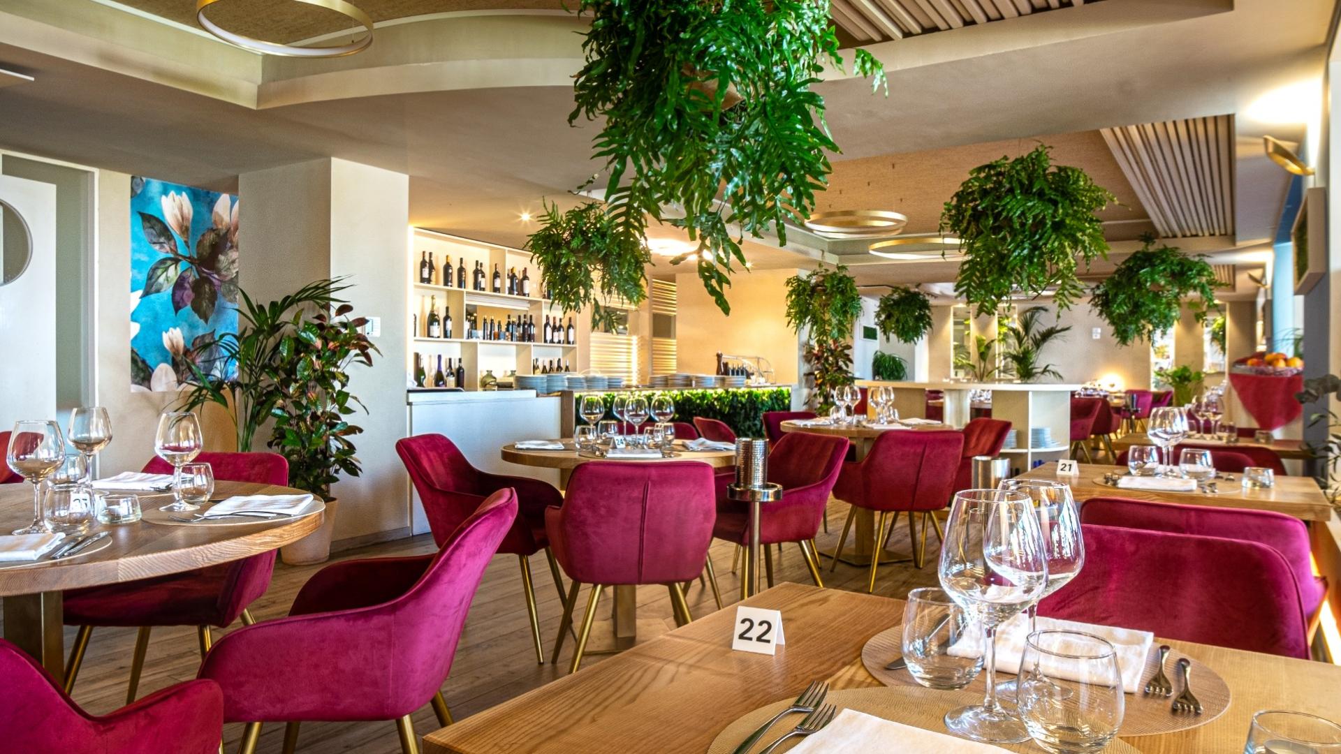 Ristorante elegante con sedie rosse, piante sospese e tavoli apparecchiati.