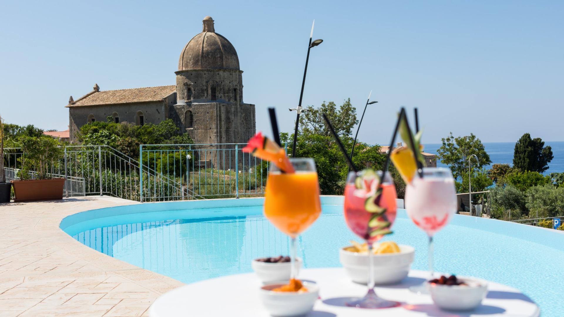 Cocktail a bordo piscina con vista su una chiesa storica e il mare.