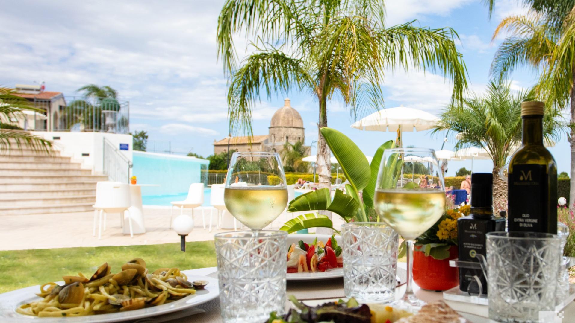 Pranzo all'aperto con vino bianco, piscina e vista su una chiesa storica.