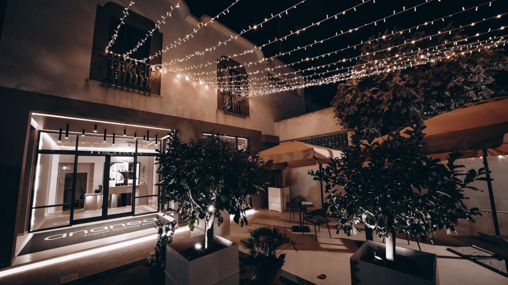 Cortile elegante con luci sospese, piante e sedie sotto ombrelloni.