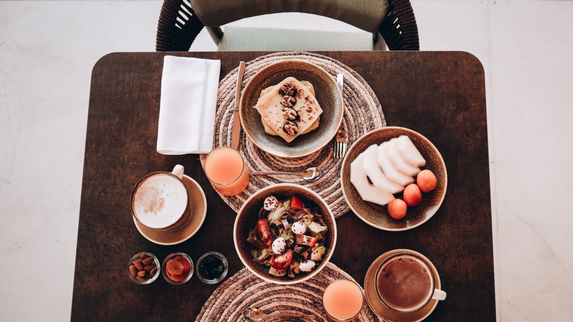 Colazione elegante con pancake, frutta, insalata, caffè e succo d'arancia su tavola apparecchiata.