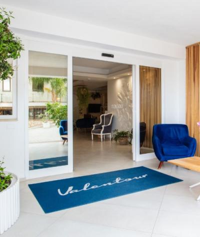 Ingresso moderno con poltrone blu e tappeto Valentour, piante decorative e tavolino di legno.