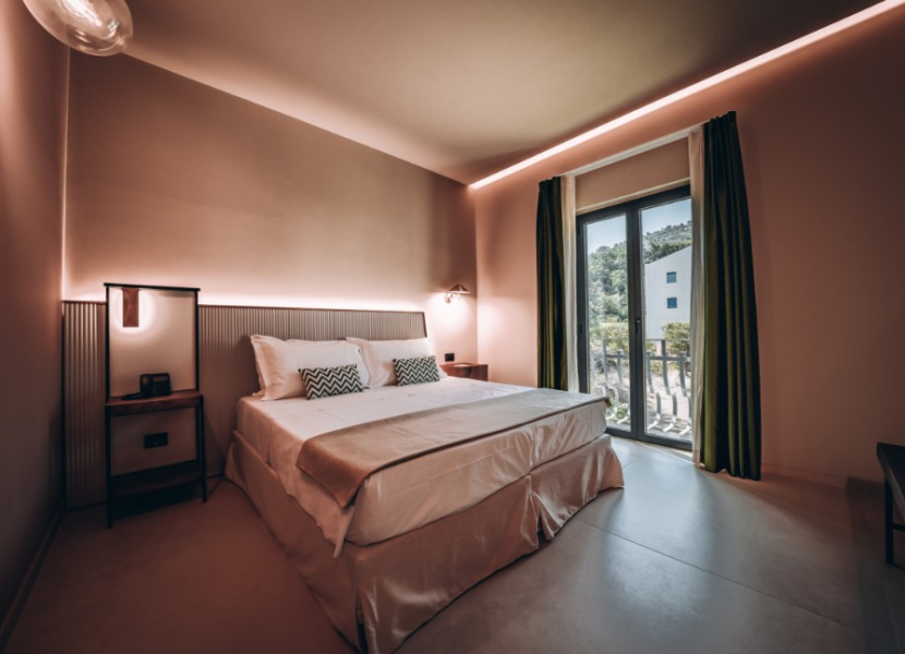 Camera moderna con letto matrimoniale, illuminazione soffusa e finestra con tende verdi.
