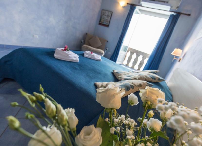 Camera accogliente, letto blu, fiori bianchi, vista sul balcone.
