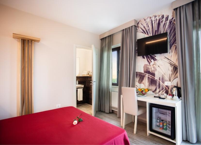 Camera moderna con letto rosso, TV, minibar e bagno.