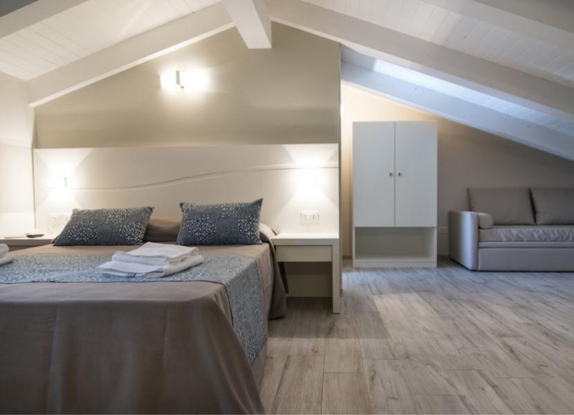 Camera da letto moderna con letto matrimoniale, armadio e divano sotto il tetto spiovente.