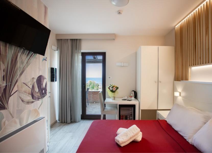 Camera moderna con letto matrimoniale, TV, balcone vista mare e decorazioni floreali.