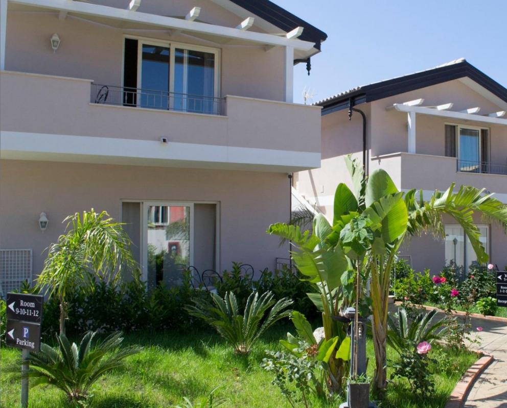 Complesso di villette moderne con giardino e segnaletica per camere e parcheggio.