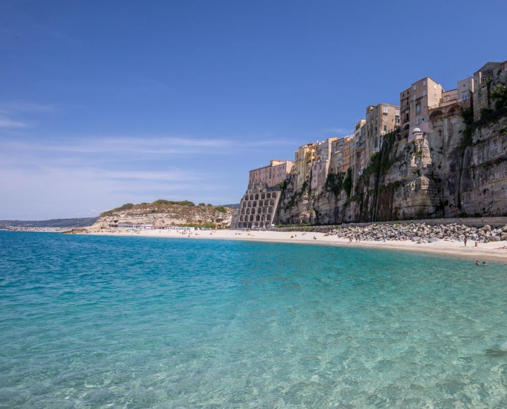 Spiaggia con acqua cristallina e case su scogliera, sotto un cielo sereno.